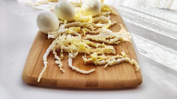 Chopped Peking cabbage and peeled eggs on cutting board as background. Cooking a healthy eco-friendly salad from natural products. Copy space and place for text