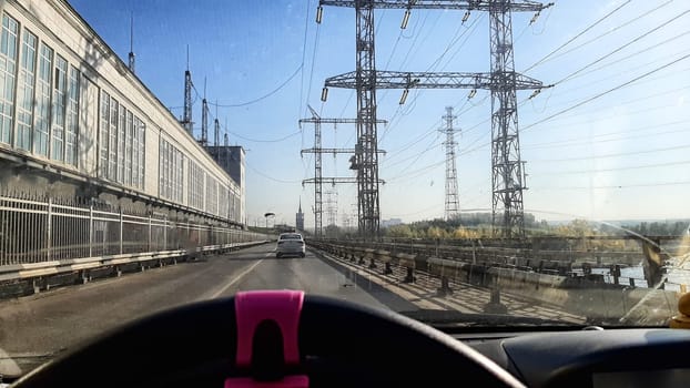 View of the hydroelectric power station, building, dam and power line from front window of car on driver's side. The concept of travel experiences. Business visit to hydroelectric power station
