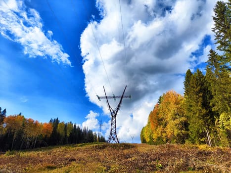 Power lines on a hill, hill or in the mountains against a blue sky with white clouds. Electric lines, towers, wires in nature landscape