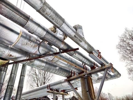 Metal pipes in thermal insulation winding outdoors and the over-illuminated white sky on background