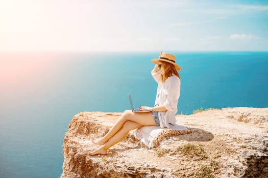 Freelance woman working on a laptop by the sea, typing away on the keyboard while enjoying the beautiful view, highlighting the idea of remote work