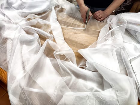 Women's hands with scissors cut the chiffon fabric. A seamstress cuts clothes. The seller prepares fabric for sale