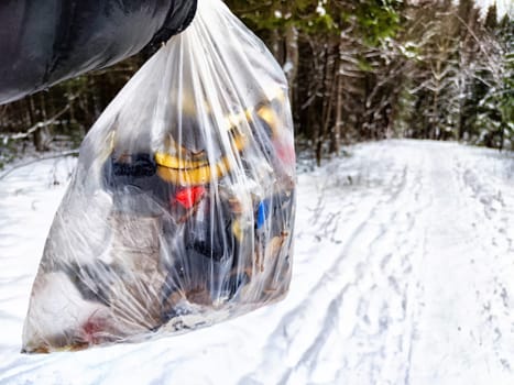 Bag of garbage in hand of woman and snow in forest on the background. A girl cleans up the trash after picnic. A tourist is going to throw garbage in nature. The concept of environmental pollution