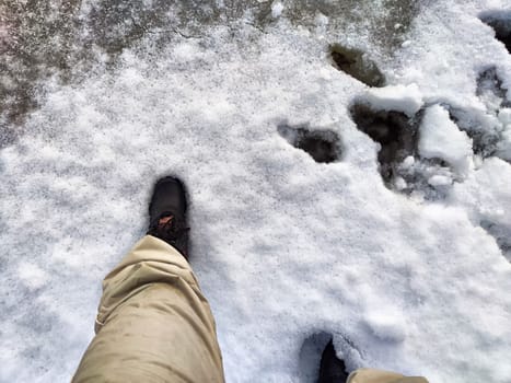 Feet of Hunter or fisherman in big warm boots on winter day on snow. Top view. Fisherman on the ice of a river, lake, reservoir on spring day with melting ice. Dangerous fishing in autumn