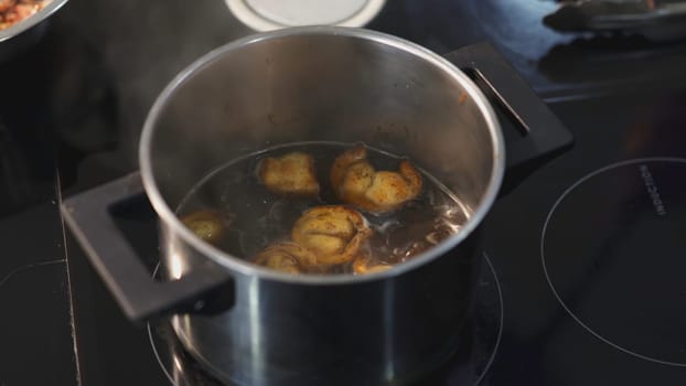 Dumplings in the broth are mixed with slotted spoon. ART. Dumplings are cooked in pot on the stove. With a ladle they caught one dumpling from the pan.