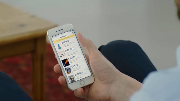 Russia, Moscow - May 2018: Purchase bitcoins with a smartphone. Stock. Close-up of a hand with a smartphone on a background of crypto currency.