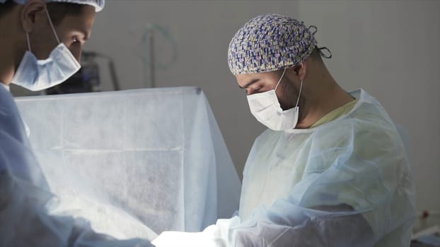 Details of a real surgery in the sterile operating theatre. Medical background of doctors wearing sterile uniform and face mask at work at the hospital.