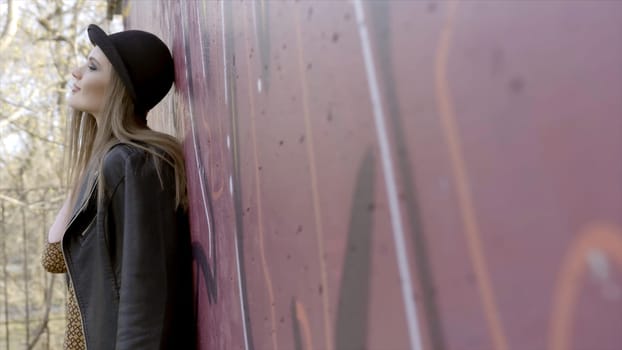 Sexy model woman in black wearing hat, standing and posing near the wall. Action. Stylish young woman in a hat standing near the wall.