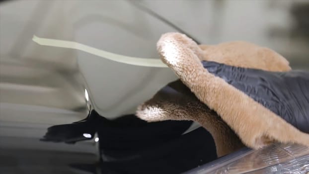 Close up for man hand in black glove washing a car window in a car wash, cleaning service. Car care service worker using microfiber cloth for cleaning a car.