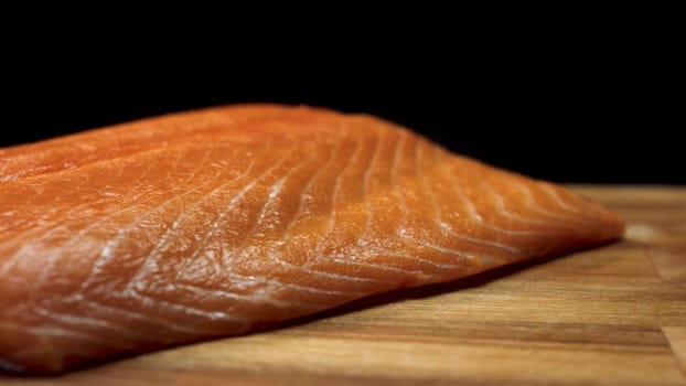 Close-up of juicy piece of salmon. Juicy fresh and red slice of salmon meat lying on wooden board on black background.