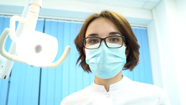 Patient point of view of a dentist examining patient mouth, modern dentistry concept. Young female dentist looking at the patient and turning the lamp.