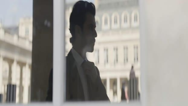 Attractive businessman in black suit thinking while standing outside on the street. Action. Man reflection in glass window near antique building