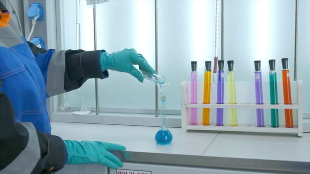 Woman conducts laboratory experiments and analyzes. Clip. Woman looks at chemical liquid in laboratory. Industrial laboratory with workers and chemicals in test tubes.