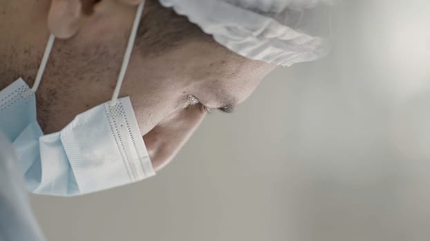 Medical surgeon in operating theater performing operation and looking down. Action. Male doctor at the hospital in mask and hat