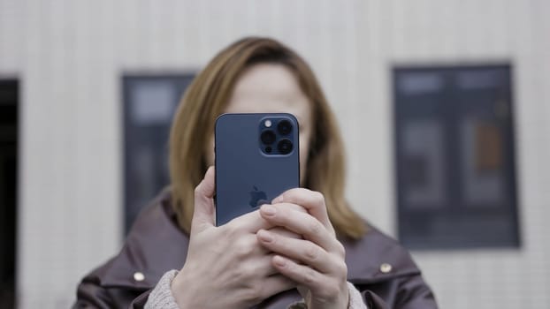 Riga, Latvia - 11.23.2020: Women taking pictures or making a video with her new device. Smiling woman with a new Apple Iphone 12 Pro Max oudoors near residential houses.