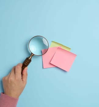 Empty paper stickers adhered to a blue background, and a female hand with a magnifying glass on a blue background