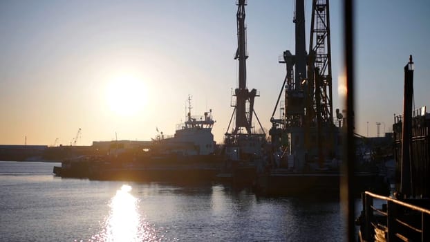 Ships standing right under the rays of the bright sun.Clip. Large ships in the river with large cargo devices stand against the background of the bright sun during the day. High quality FullHD footage