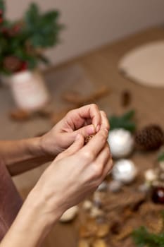 Female hands creating Christmas craft handmade decor with fir branches.