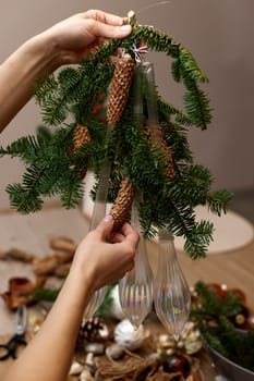 Woman making Christmas arrangement with fir branches, pine cones and bow. craft handmade decor.