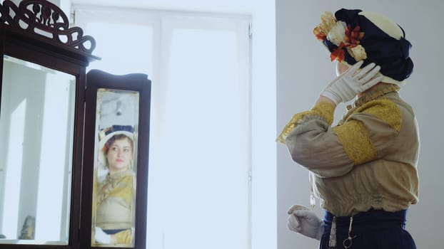 Woman in antique outfit. Stock footage. Woman in 19th century outfit looks in mirror. Woman in antique dress and hat looks in mirror. Theater and costumes.