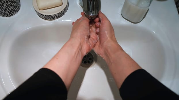 Woman washing hands with soap in bathroom. Close up of female hands turning on the tap and taking soap for corona virus prevention, hygiene to stop spreading coronavirus.