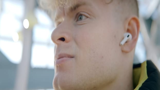 Close-up of man with headphones on street. Action. Young man with headphones looks into distance. Inspiring music in headphones on sunny day.