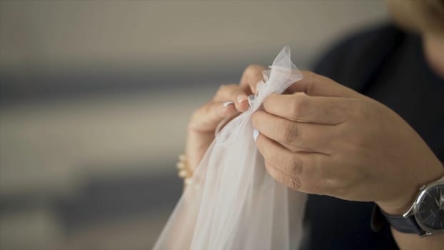 Close-up of old hands sewing white fabric. Action. Beautiful women's hands manually sew white transparent fabric with needle. Woman sews by hand thin fabric for veil.