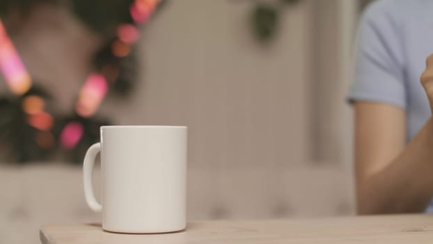 Close-up of women's hands pouring tea on background of lights. Stock footage. Young woman makes herself cup of tea. Woman makes tea on background of blurred lights.