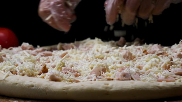 A female hands in cooking gloves sprinkling pizza with grated cheese, italian food concept. Close up for chef hands putting cheese on the pizza.