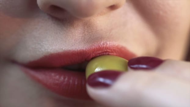 Close up of red sexy lips of a woman biting a green olive. Sensitive red lips, extreme close up of facial details of a young woman with beautiful skin.