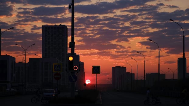 Early morning sunrise in a city street. Breathtaking pink and orange sky with bright red shining sun rising above the dark city with walking people and driving cars.