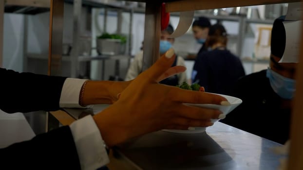 Germany - Berlin, December 15, 2023: In the restaurant, the waiter takes the prepared dish from the chef. Media. Plate with food on the metal surface at the cafe, cooks at work on the background
