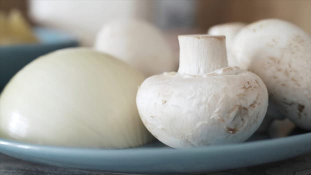 Close up of fresh mushrooms and cut onion lying on glass plate. White raw champignons and onion, ingredients prepared for cooking, food concept.