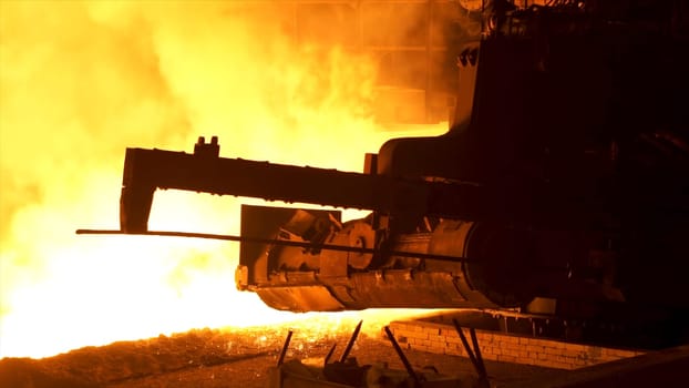 Molten metal pouring from the special mechanism, metallurgy concept. Molten steel flowing in metallurgical chute behind moving mechanism
