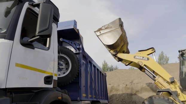 Germany - Berlin, November 20, 2022: Excavator in action at the construction site. Scene. Excavator flipping the bucket of yellow color loaded with sand, loading the truck with sand