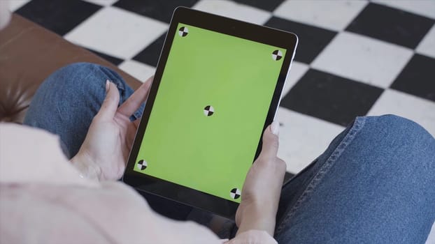 Young brunette woman watching her tablet with green screen on black and white floor background. Side view of a girl using tablet pc with chroma key.
