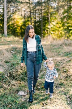 Little girl walks along a green lawn in the forest holding her mother hand. High quality photo