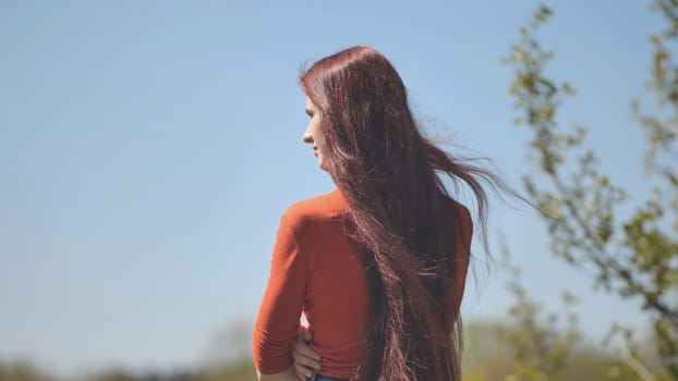A girl with burgundy long hair admiring nature on a summer day