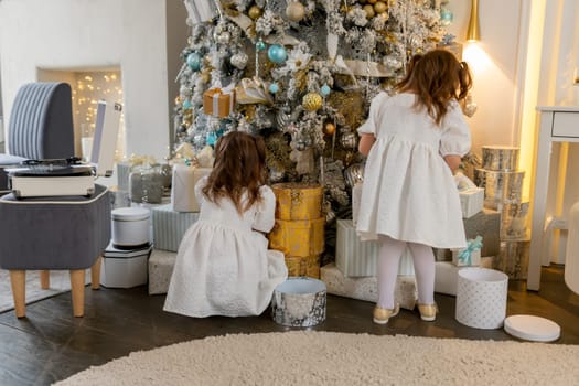 Two twin sisters in a white dress decorate the Christmas tree with their own hands, Christmas holidays at home