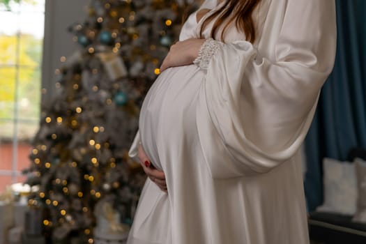 Pregnant woman holding a belly against Christmas tree with lights. family holiday concept