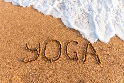 The inscription yoga on the sea sand, the concept of a wellness tour. sea with sand, top view, inscription.