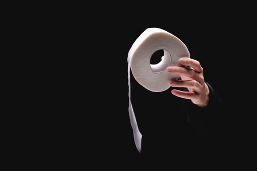Close-up of a woman's hand using toilet paper, against a dark background. A hand holds a roll of paper. White roll of toilet paper in a woman's hand.
