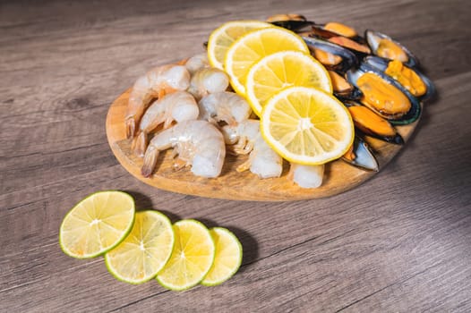 Mussels in shells, shrimps in shell with lemon lying on a wooden table on a wooden flat plate, close-up appetizer.