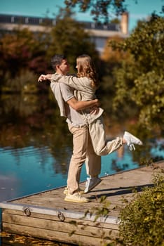 A happy couple in love in casual clothes travel together, hike and have fun in the fall forest on a weekend in nature in autumn outdoors, selective focus. Handsome man embracing with passion his girlfriend outdoor under the leaves of trees on the embankment. Love history. Happy people concept