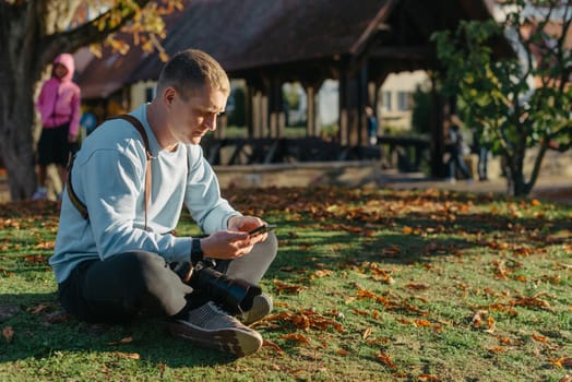 Professional photographer taking picture of beautiful autumn park. man professional photographer sit with camera in autumn park