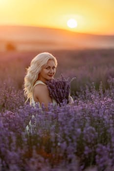 Blonde woman poses in lavender field at sunset. Happy woman in white dress holds lavender bouquet. Aromatherapy concept, lavender oil, photo session in lavender.