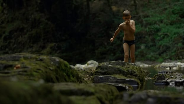 Boy walking on mossy rocks on green hills background. Creative. Teenager boy in jungles
