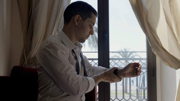 Young businessman getting dressed in formal suit in a hotel room. Action. Young man in white shirt indoors