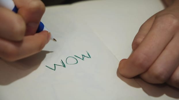 Close up of hand writing words on white paper with a pen. Child is writing a word mom on a sheet of paper.