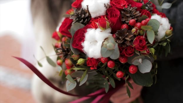 Close up of a bride holding a wedding bouquet with red roses. Bride holding flowers.